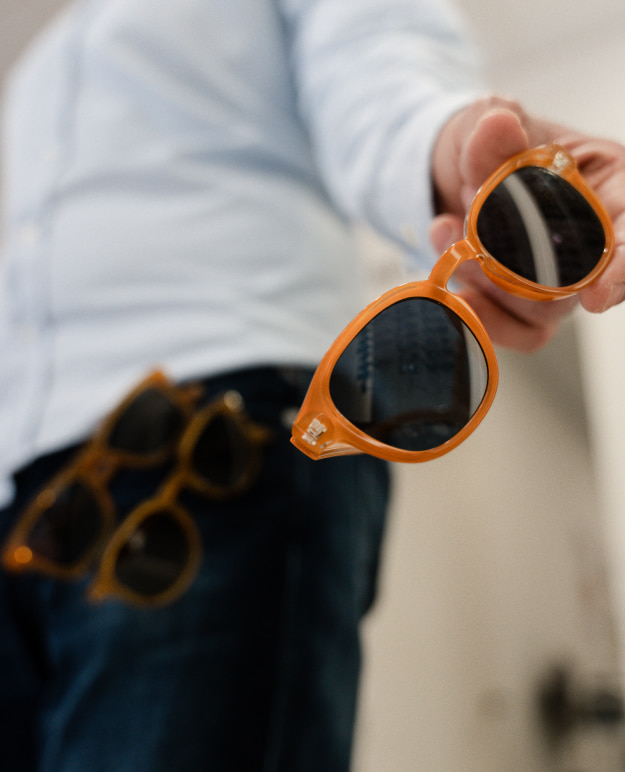 Hombre sujetando gafas de sol naranjas